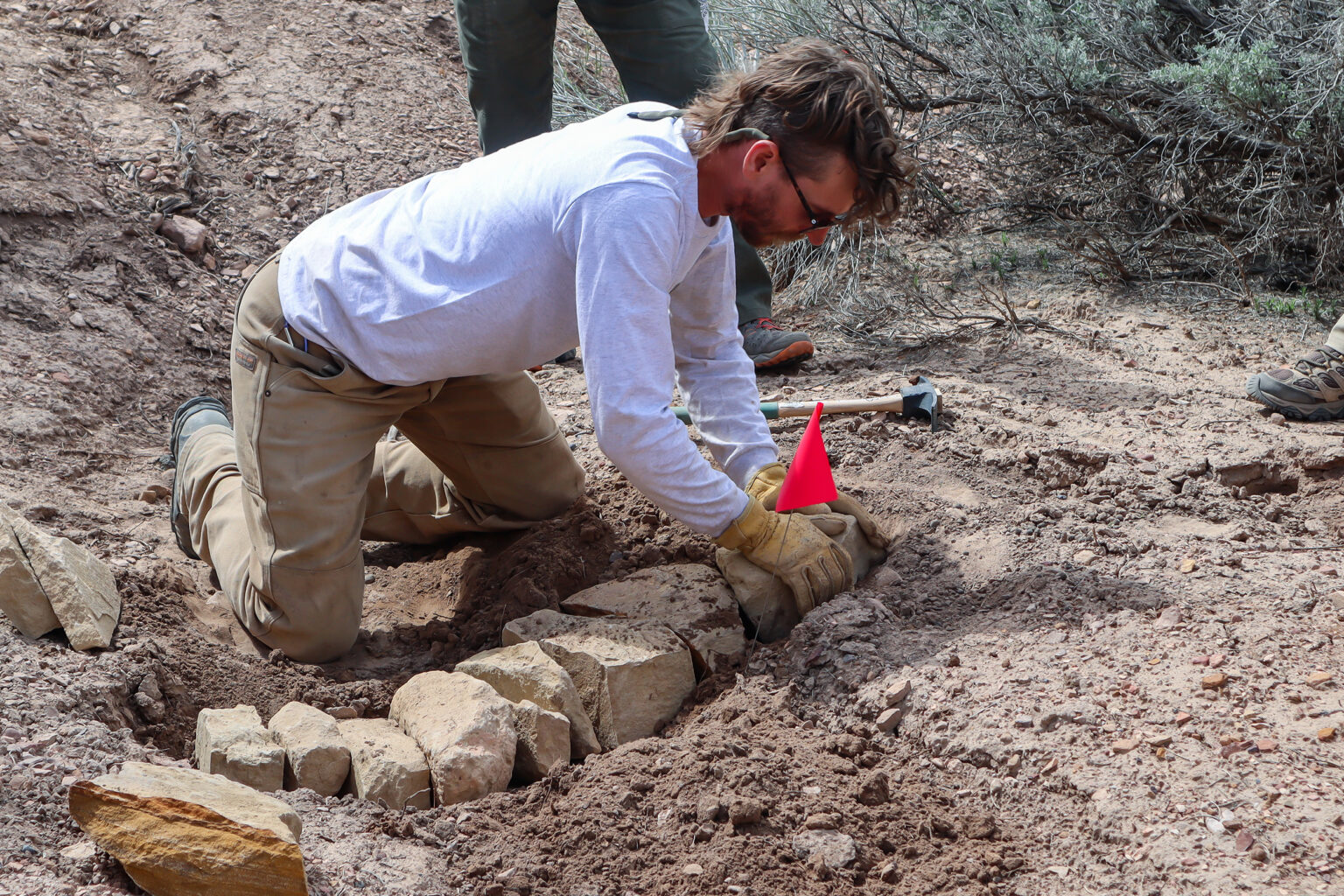 A man kneels on the ground and does rock work.