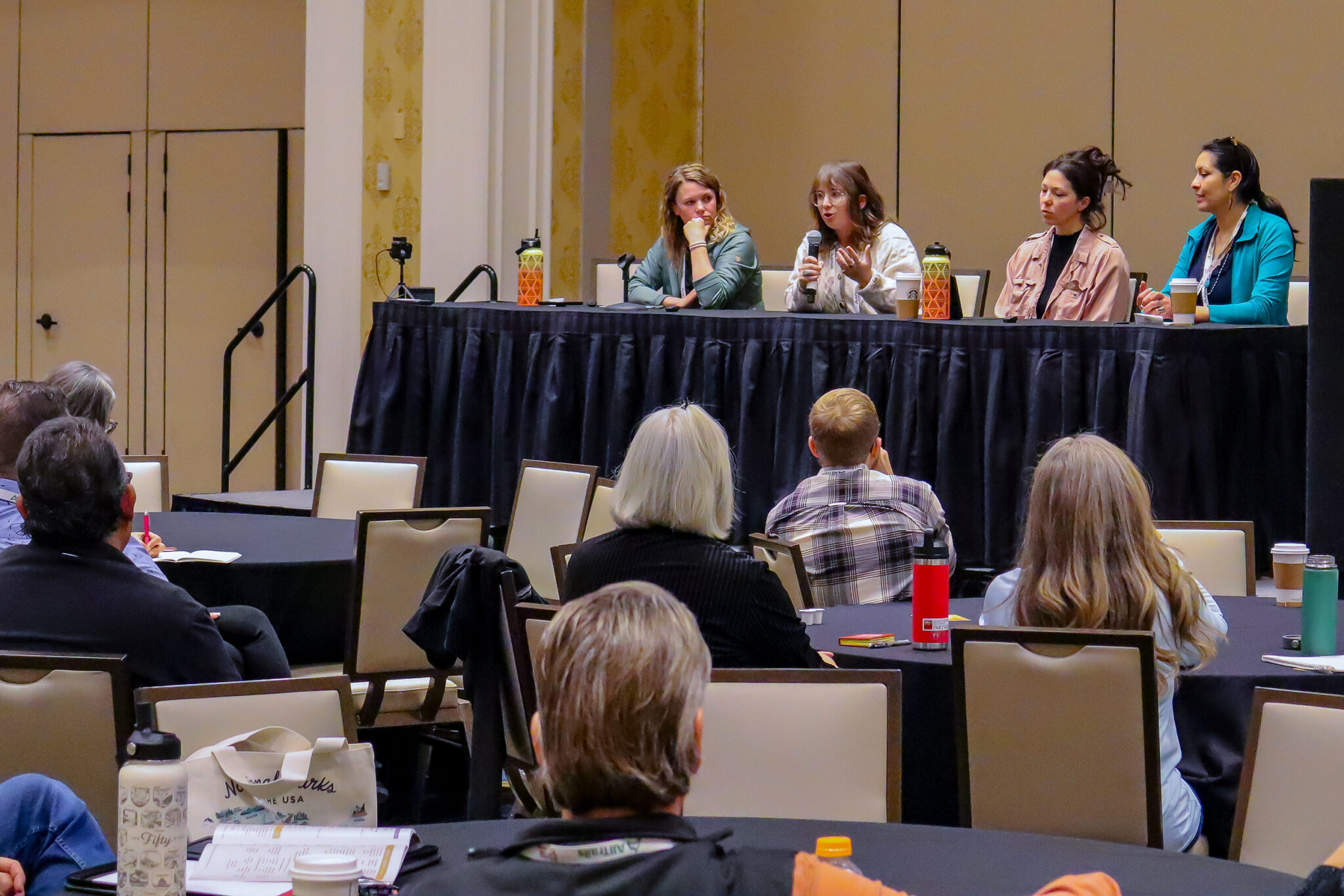 A woman speaks on a panel of women to an audience in a conference-type room