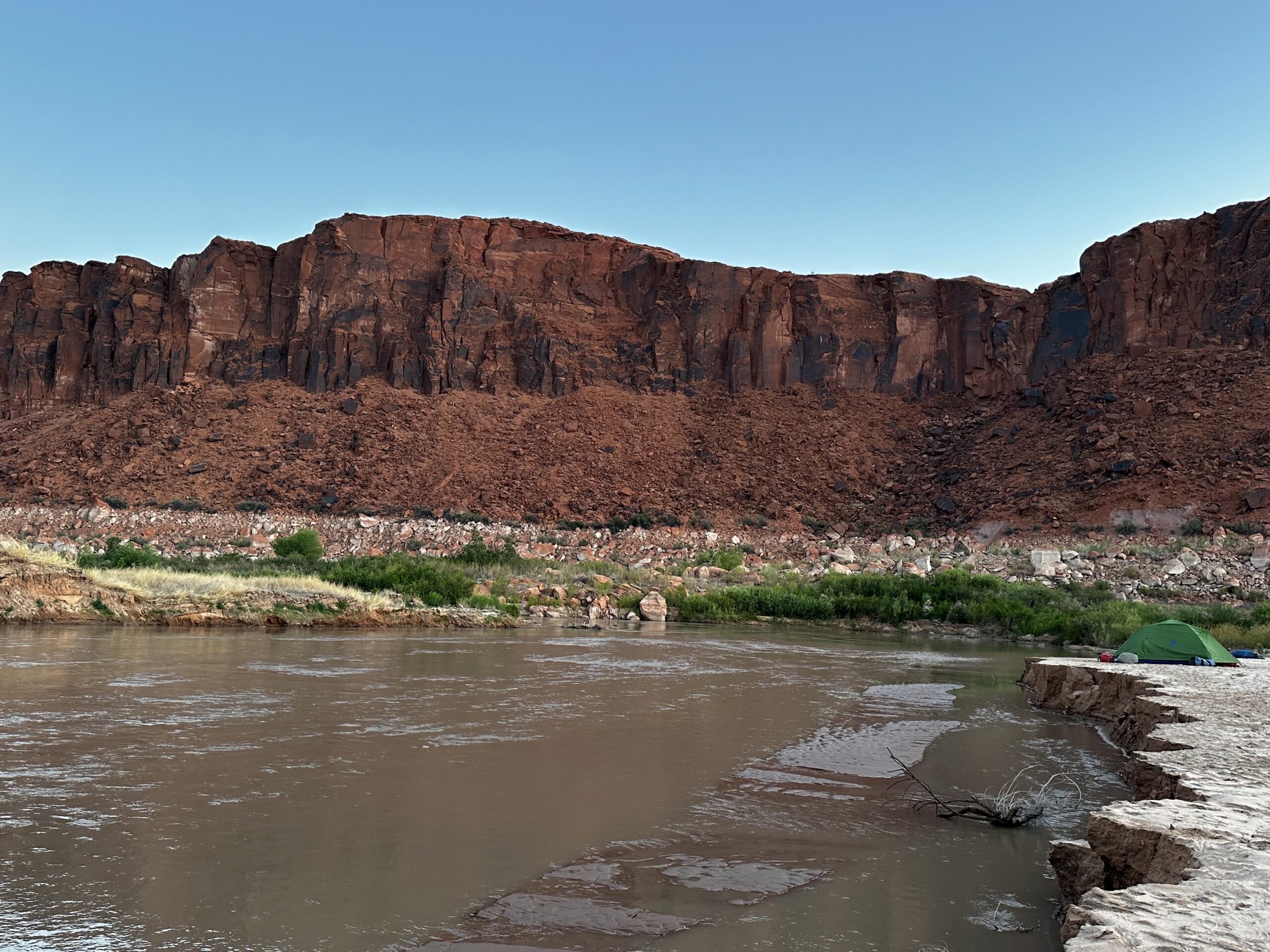 A desert waterway with red rock in the background.