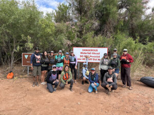 A group poses with a "Dangerous Waterfall Ahead" sign at a boating put in.