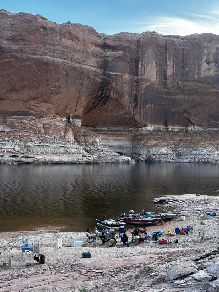 Boaters camping at the banks of a waterway with a bathtub ring on the sandstone in the background.