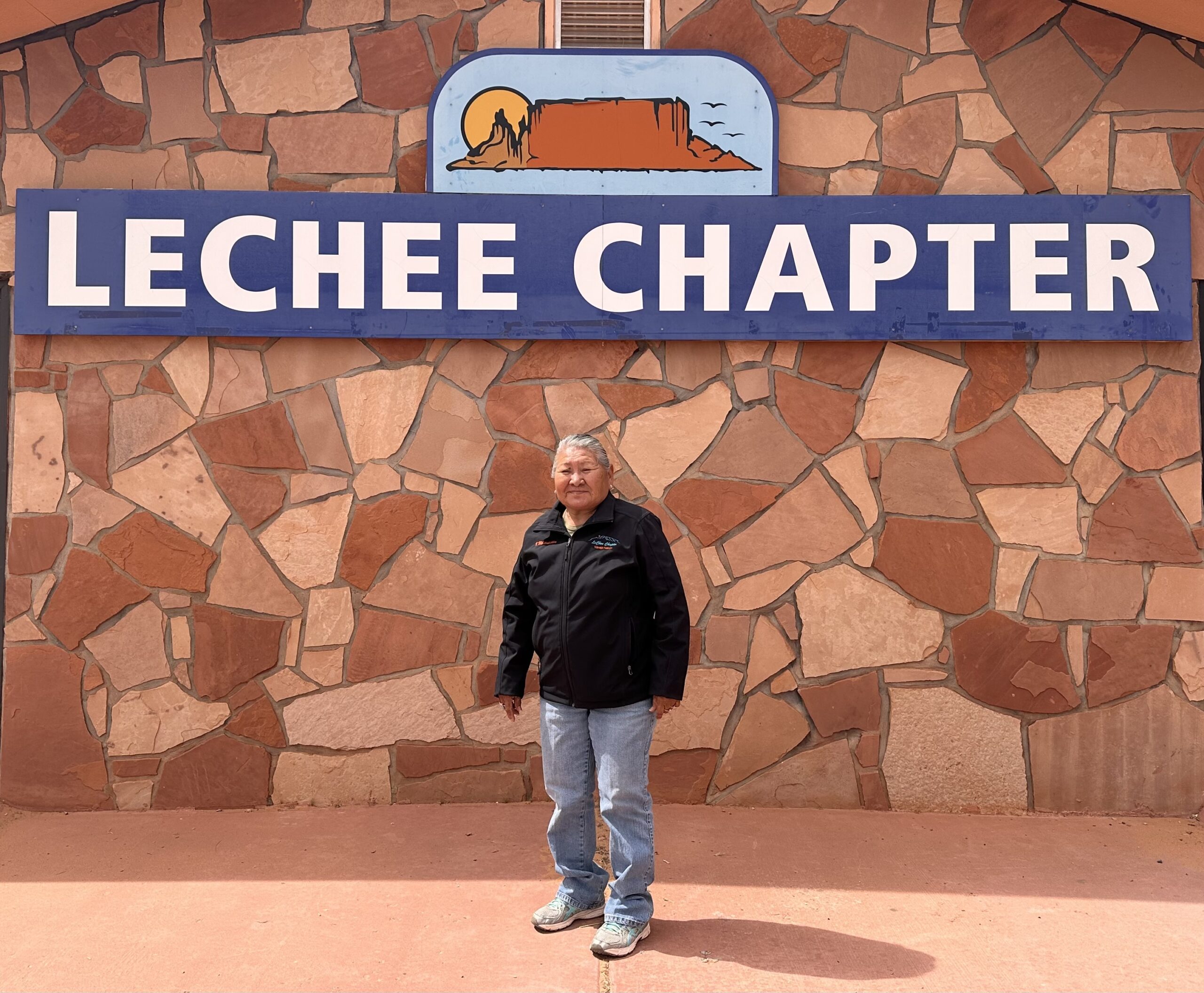 A man stands in front of a stone wall with the words "Lechee Chapter."