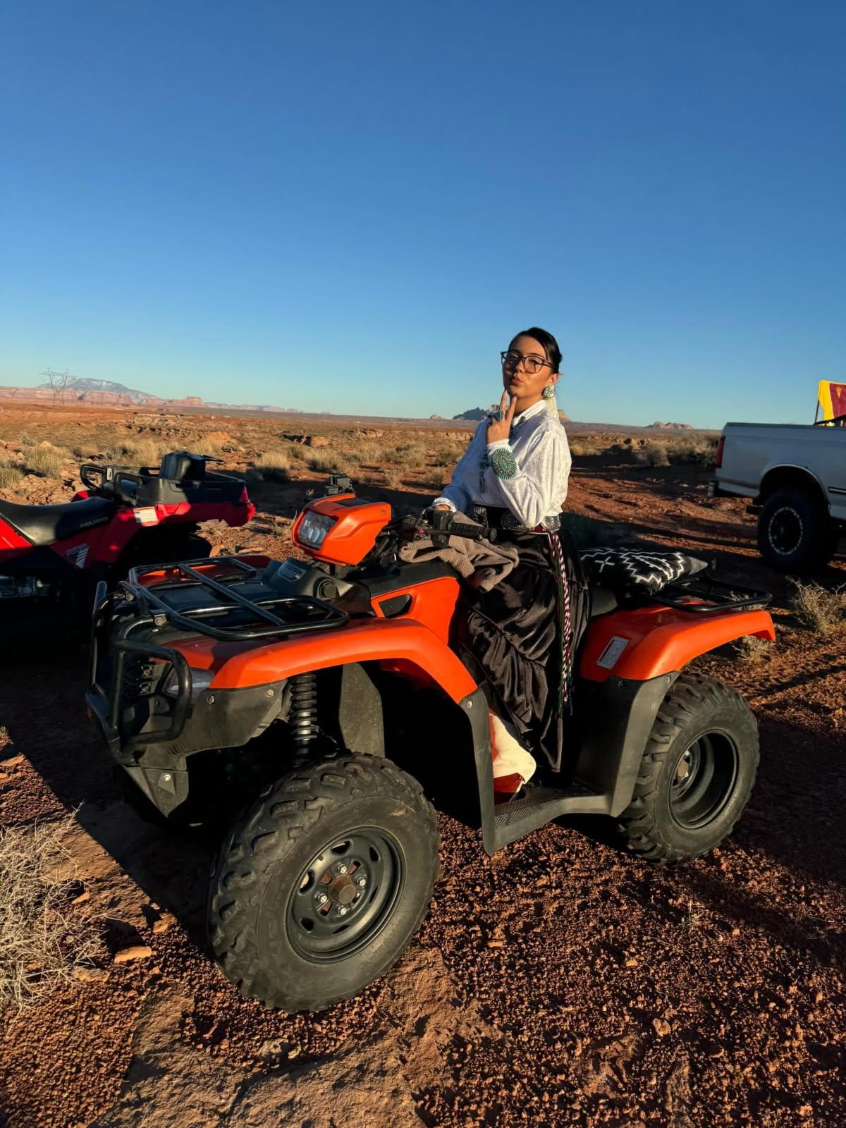 A young girl posing on an ATV in a desert landscape.